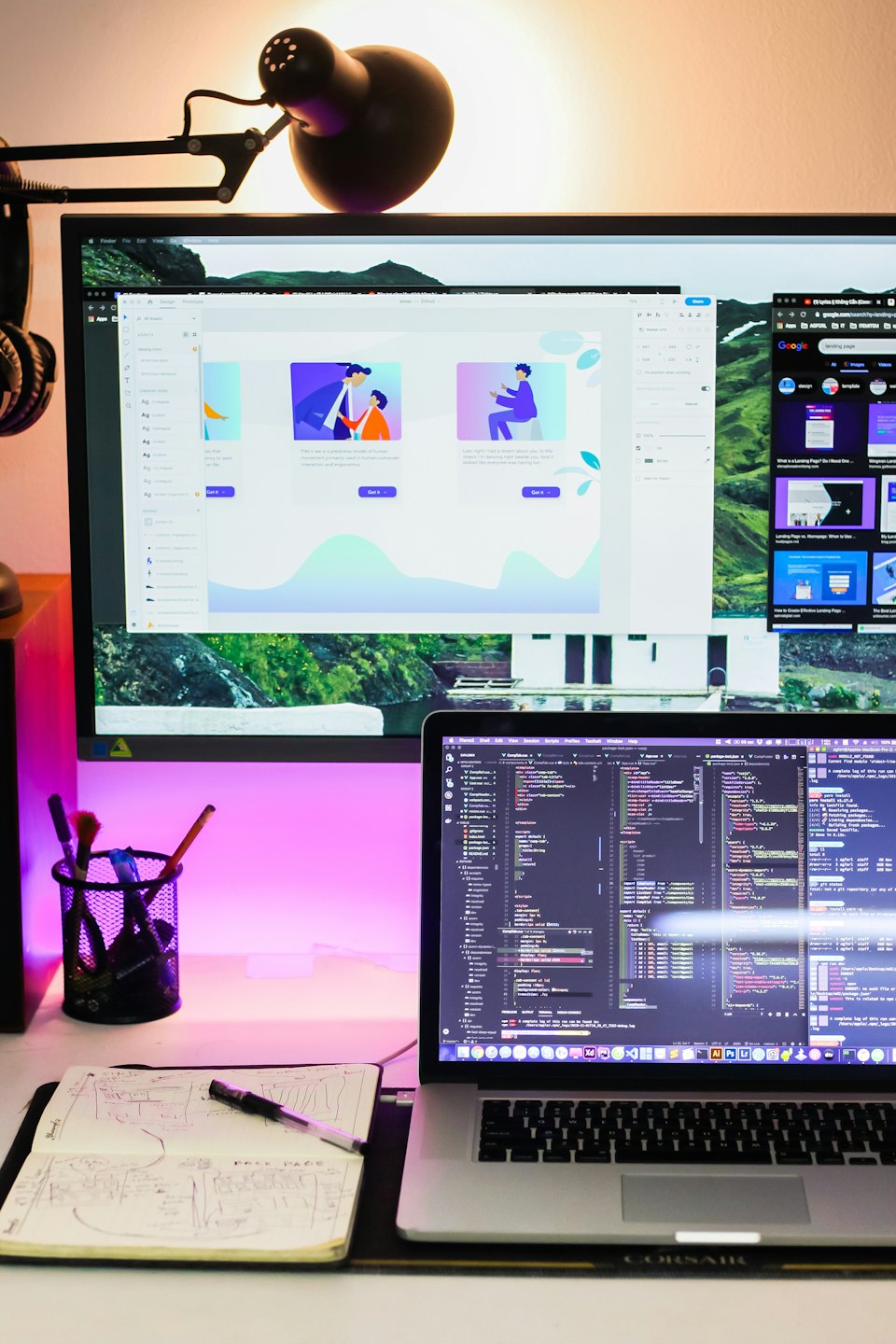 Una scrivania moderna con monitor, laptop e taccuino.